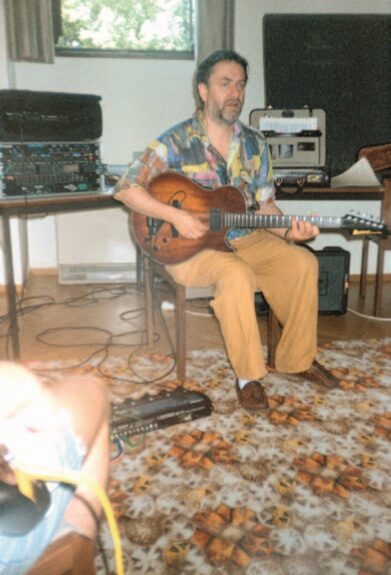 Harry Pepl sitzt mit seiner Gitarre auf einem Stuhl, hinter ihm ein Rack mit Effektgeräten und ein Verstärker, vor ihm auf dem Teppich ein Effektboard; links vorne angeschnitten eine weitere Person. Beim Unterrichten an der Kunstuniversität Graz (Auskunft Daniel Pepl, 19.10.2026). Das Foto erschien in Martin Schaberls Hochschulschrift über Wolfgang Muthspiel (Kunstuniversität Graz, 2004, S. 165).